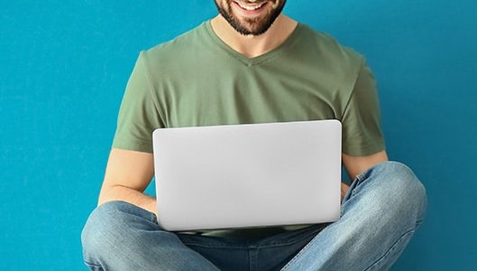 Thumbnail image of online learning student cross-legged with laptop against a blue background - researching online business courses